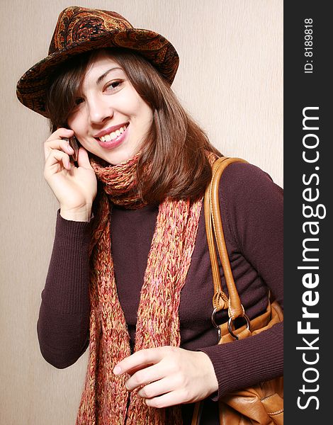 The girl in a felt hat and an orange scarf speaks by phone. The girl in a felt hat and an orange scarf speaks by phone.