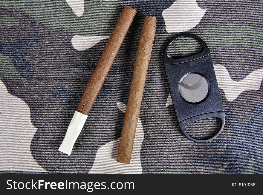 Cigars on a camouflaged jacket, with a cigar cutter.