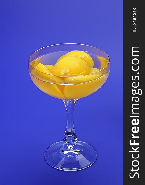 Halves of peaches in light syrup in a glass  on a dark blue background. Halves of peaches in light syrup in a glass  on a dark blue background