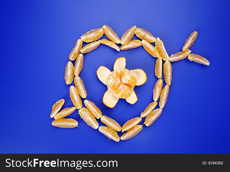 Slices of a tangerine stacked as the heart pierced with an arrow, on a dark blue background. The concept of love. Slices of a tangerine stacked as the heart pierced with an arrow, on a dark blue background. The concept of love.