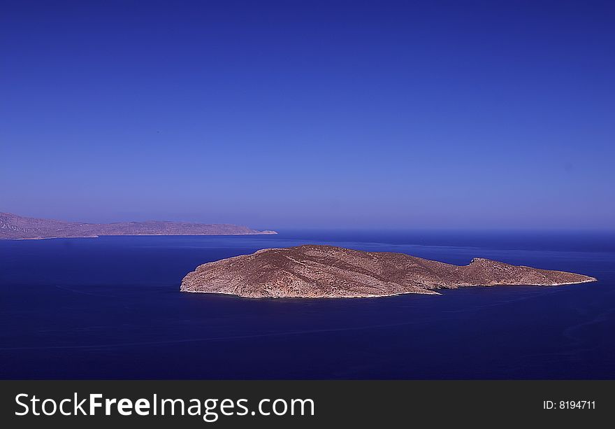 An image of shore of Crete with lonely island immersed in blue water