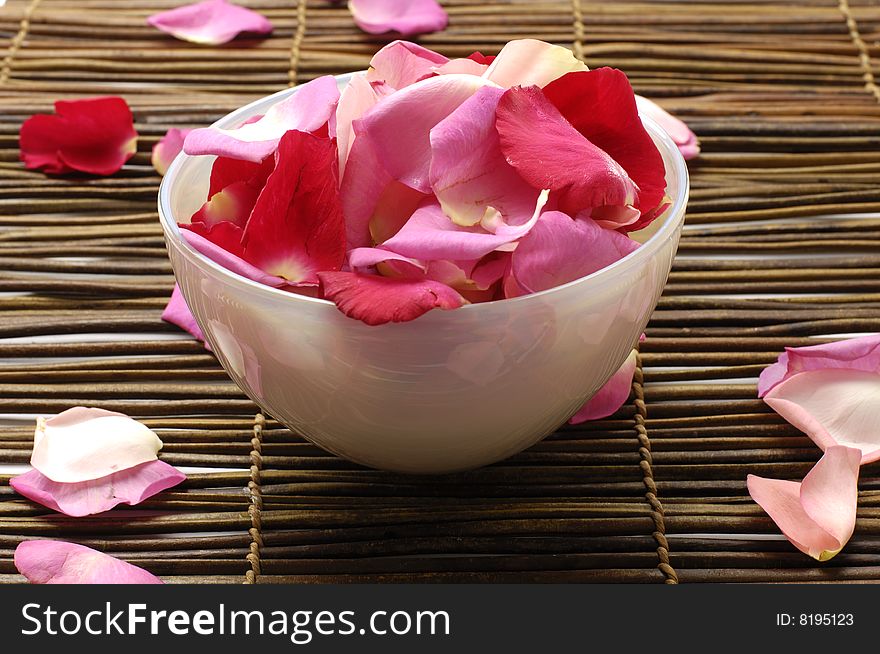 Rose petal floating in water in bowl sitting on bamboo mat. Rose petal floating in water in bowl sitting on bamboo mat