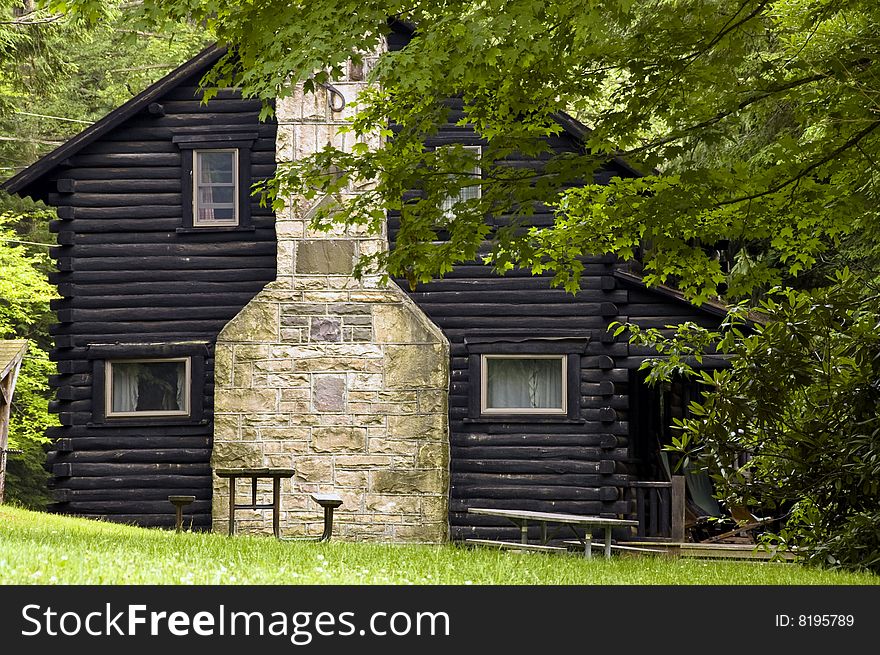 A log cabin side view, surrounded by trees in summer. A log cabin side view, surrounded by trees in summer