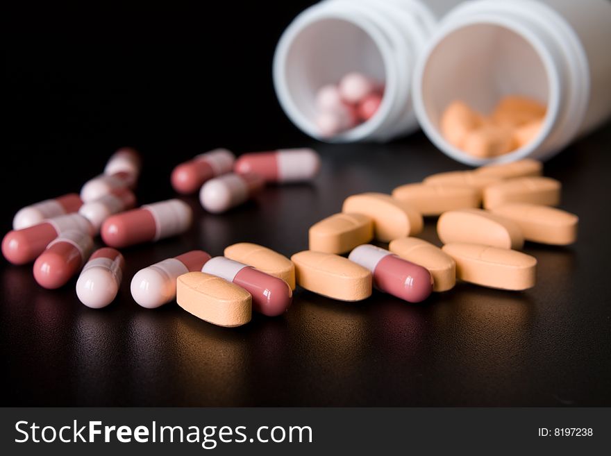 Picture of plastic bottles with lot of pink and orange pills on table. Picture of plastic bottles with lot of pink and orange pills on table