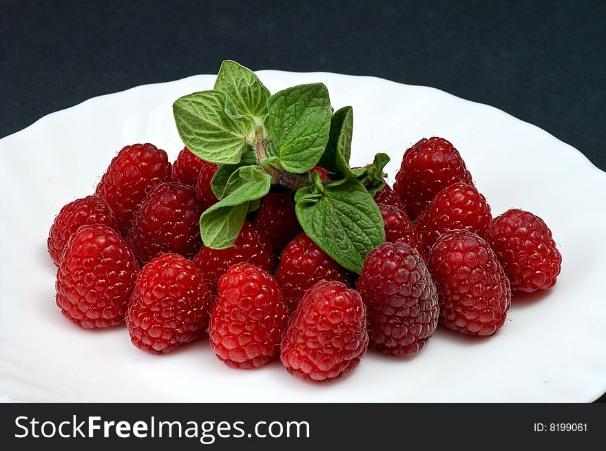 Fresh ripe raspberry whith mint leaves on white porcelain plate