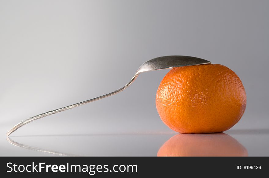 Copper teaspoon leaning a tangerine, reflective surface