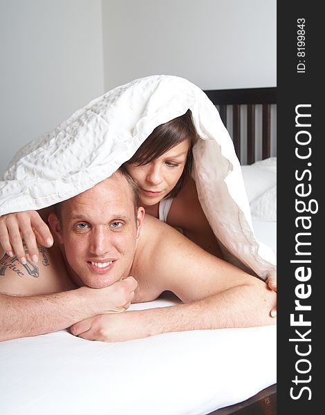 Young couple in their bed. They are playing in romance under the sheets. Young couple in their bed. They are playing in romance under the sheets.