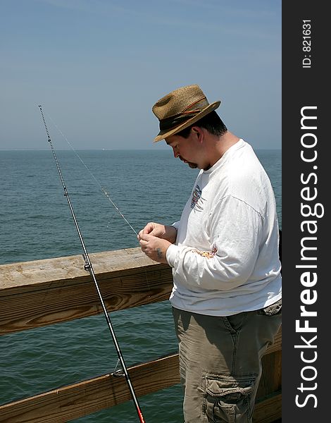 A man baiting a fishing hook on a fishing pier. A man baiting a fishing hook on a fishing pier.