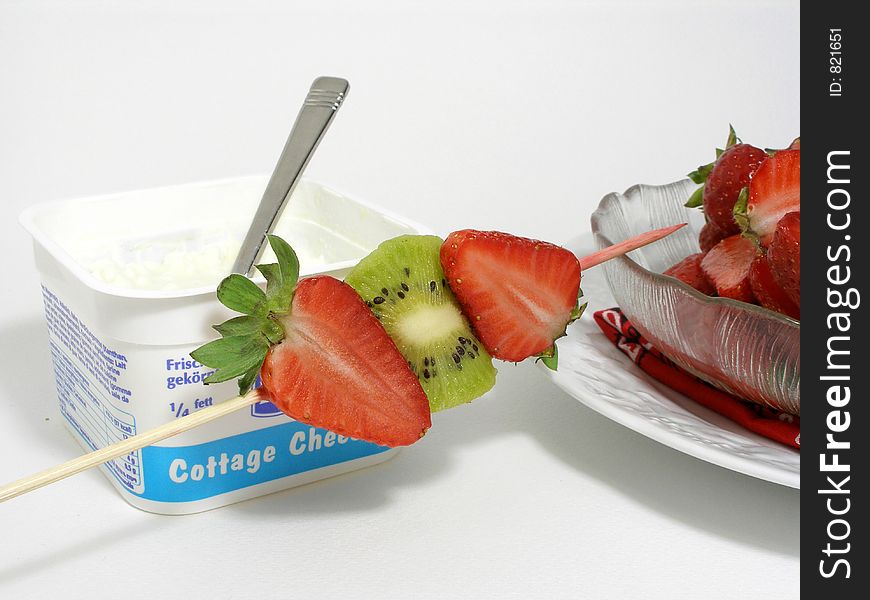 Cottage cheese in its plastic container with a fruits skewer and a bowl of strawberries. Cottage cheese in its plastic container with a fruits skewer and a bowl of strawberries