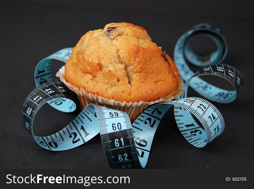 This is an image of blueberry muffin and a measuring tape. This is a metaphor for dieting. This is an image of blueberry muffin and a measuring tape. This is a metaphor for dieting.