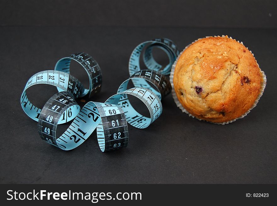 This is an image of a blueberry muffin and a measuring tape. This is a metaphor for dieting. This is an image of a blueberry muffin and a measuring tape. This is a metaphor for dieting.