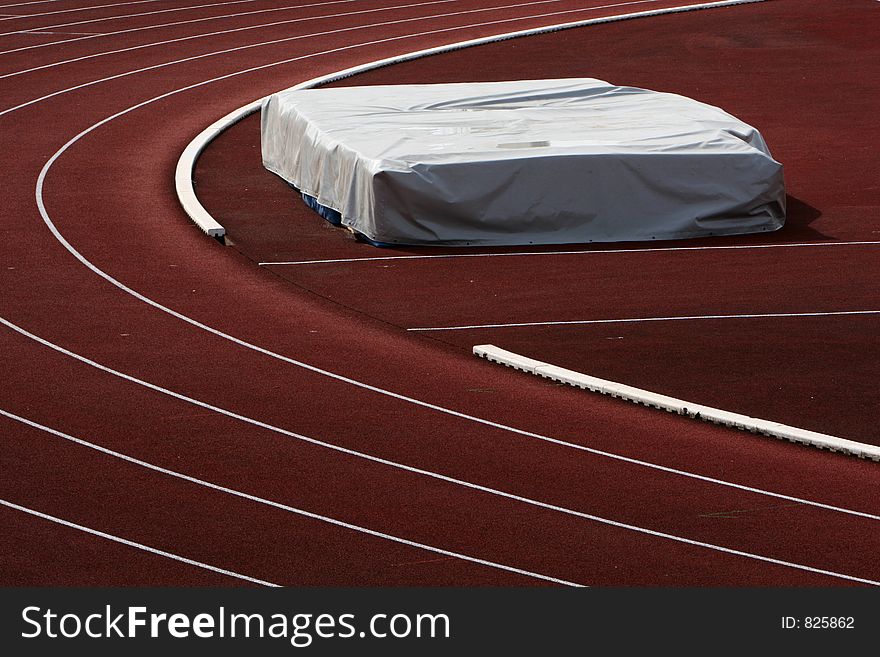 Shot of red running track with white lines and a jumping mattress on the sideline. Shot of red running track with white lines and a jumping mattress on the sideline