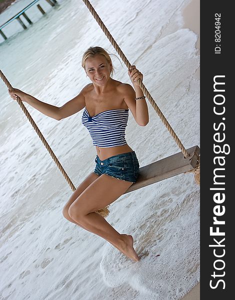 Blond girl on rope swings at the beach
