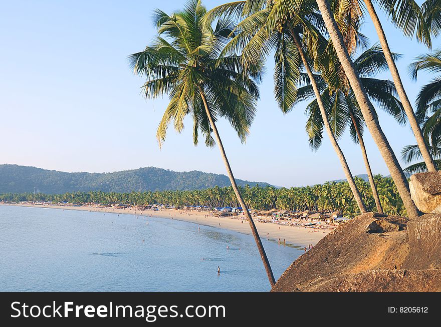 Palm trees with beautiful seascape on background with mountains, bay, sand beach and shacks. Palm trees with beautiful seascape on background with mountains, bay, sand beach and shacks.