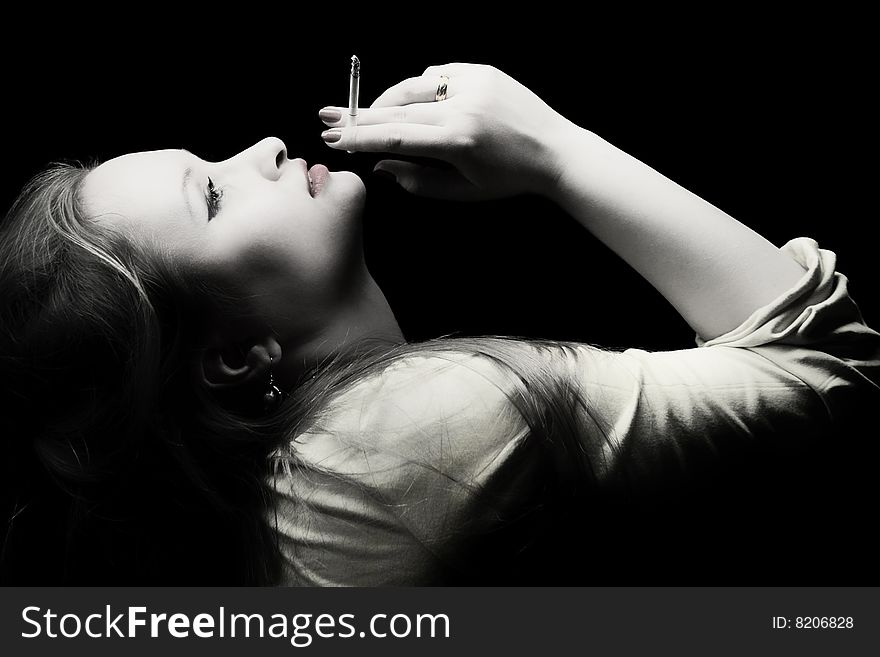 Portrait of beautiful young woman with a cigarette in a hand on a black background