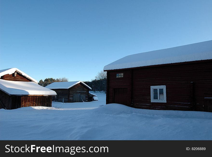 Swedish farm in winter, with barn and a clear blue sky.