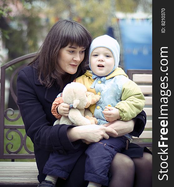 A young mother sitting on a park bench with her baby child in her arms. A young mother sitting on a park bench with her baby child in her arms.