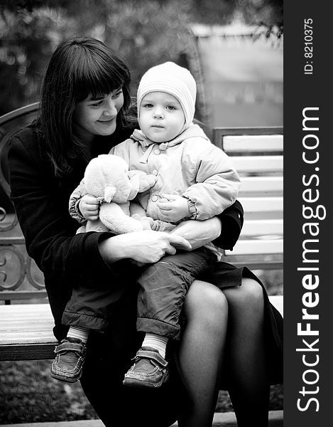 A young mother sitting on a park bench with her baby child in her arms. A young mother sitting on a park bench with her baby child in her arms.