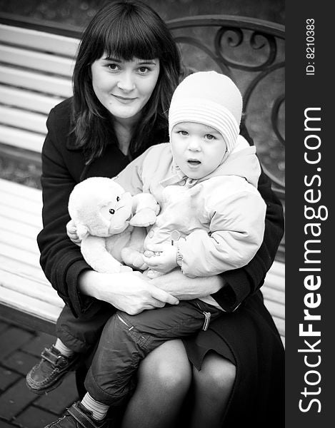 A young mother sitting on a park bench with her baby child in her arms. A young mother sitting on a park bench with her baby child in her arms.