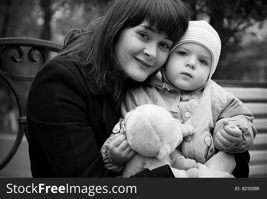 A young mother sitting on a park bench with her baby child in her arms. A young mother sitting on a park bench with her baby child in her arms.