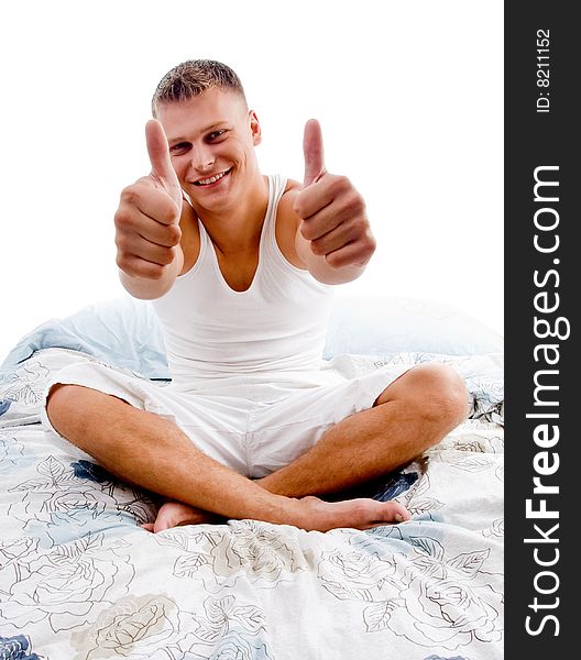 Sitting young man showing thumb up with both hands in bed