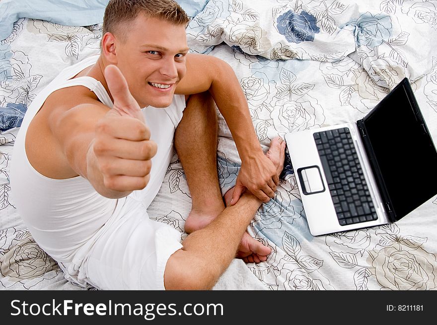 Young man with thumbs up and laptop in bed