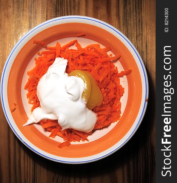 Grated carrots with honey and sour cream in a salad dish with an orange border