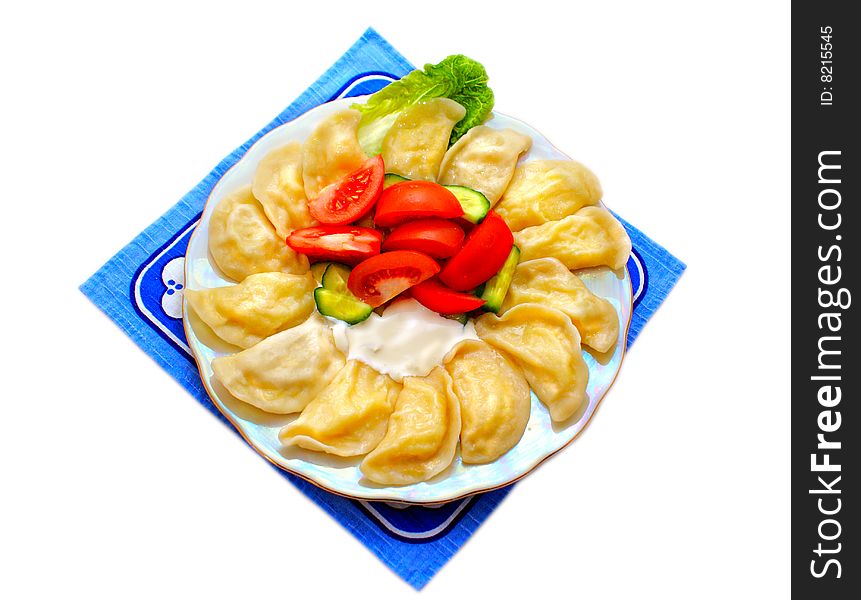 At the plate, laid in a circle of dough products with filling. Russian-Ukrainian national dish of dough stuffed potatoes with fresh vegetables, fat sour cream. White background. At the plate, laid in a circle of dough products with filling. Russian-Ukrainian national dish of dough stuffed potatoes with fresh vegetables, fat sour cream. White background.