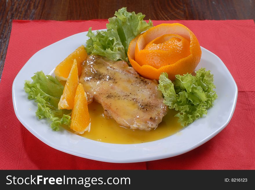 A plate of juicy pork chop with green salad, decorated with slices of orange and citron shaped as a rose. A plate of juicy pork chop with green salad, decorated with slices of orange and citron shaped as a rose