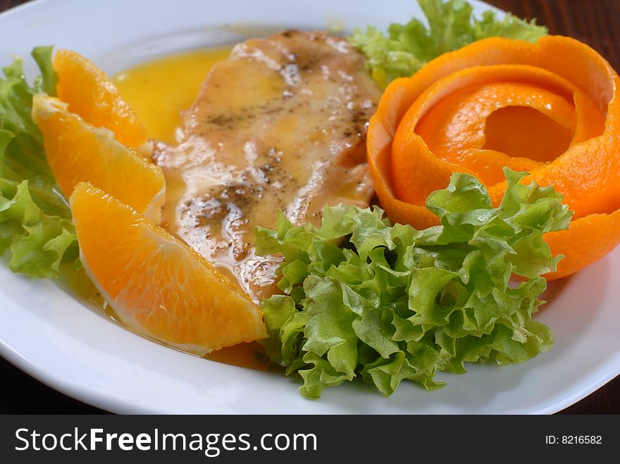 A plate of juicy pork chop with green salad, decorated with slices of orange and citron shaped as a rose. A plate of juicy pork chop with green salad, decorated with slices of orange and citron shaped as a rose