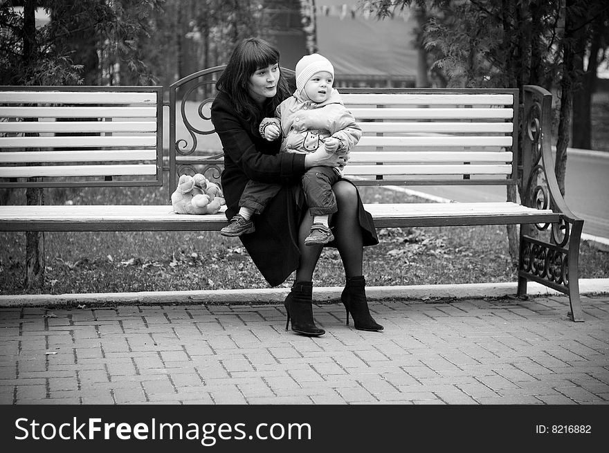 A young mother sitting on a park bench with her baby child in her arms. A young mother sitting on a park bench with her baby child in her arms.