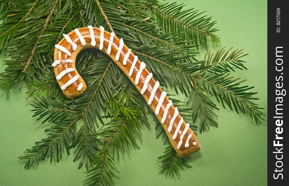 Candy cane cookie with fir branch isolated on green paper. Candy cane cookie with fir branch isolated on green paper