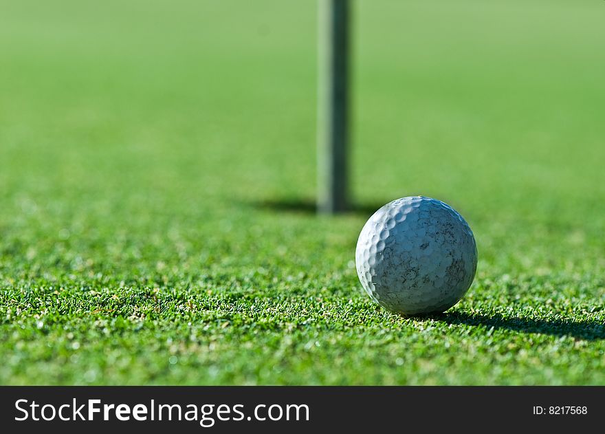 A close up of an old scuffed up golf ball on the green with the hole and flag in the background. Narrow depth of field. A close up of an old scuffed up golf ball on the green with the hole and flag in the background. Narrow depth of field.