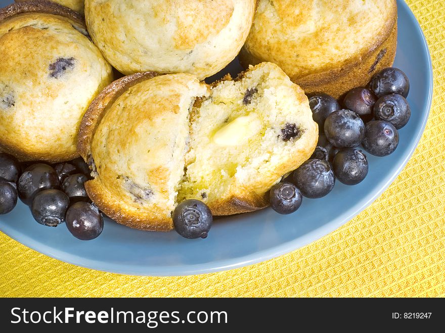 Fresh Blueberry Muffins with melting butter on a blue plate with yellow background  copy space. Fresh Blueberry Muffins with melting butter on a blue plate with yellow background  copy space
