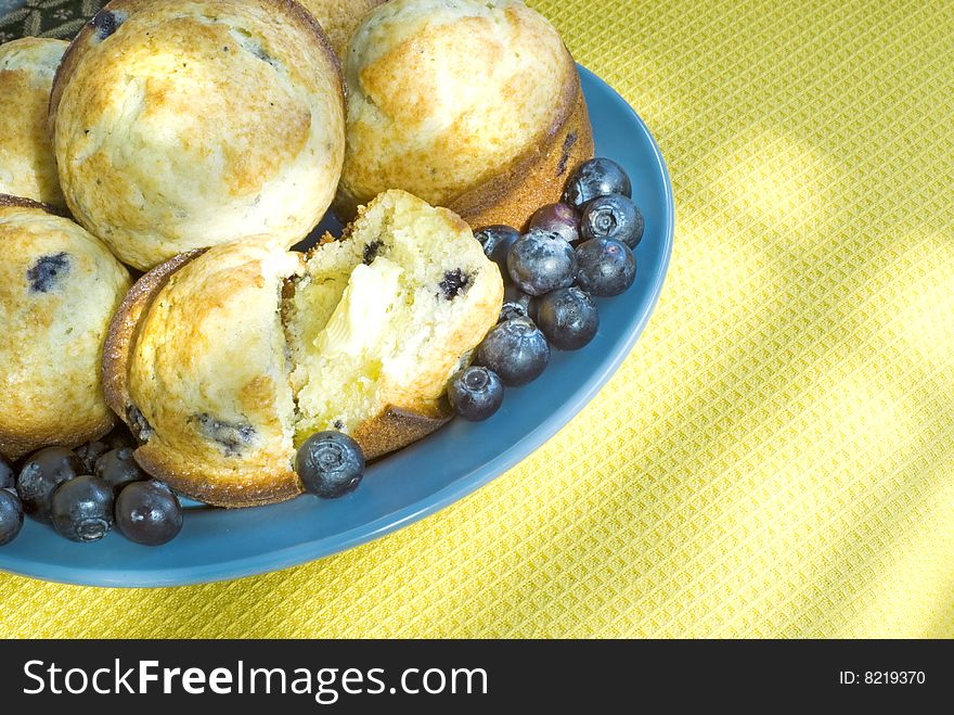 A plate of hot blueberry muffins with butter by a sunny window  copy space. A plate of hot blueberry muffins with butter by a sunny window  copy space