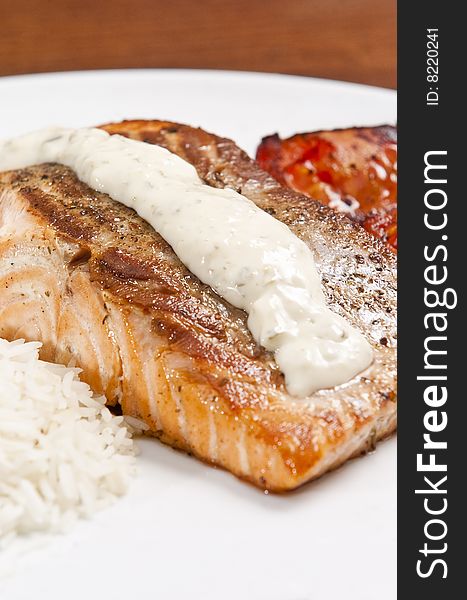 Cooked salmon fillet on white plate with rice and tomato