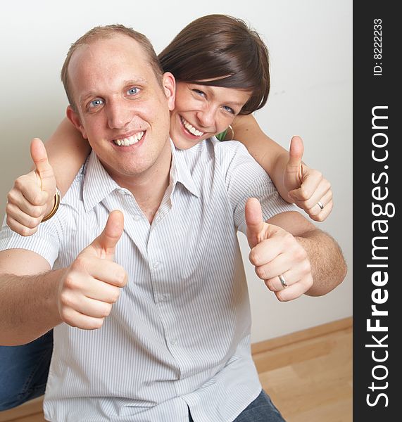 A young couple in love shows a thumbs up sign in their new appartment.