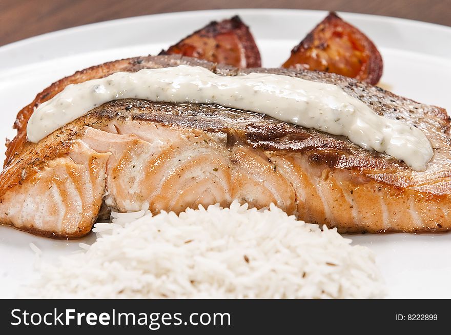 Cooked salmon fillet on white plate with rice and tomato