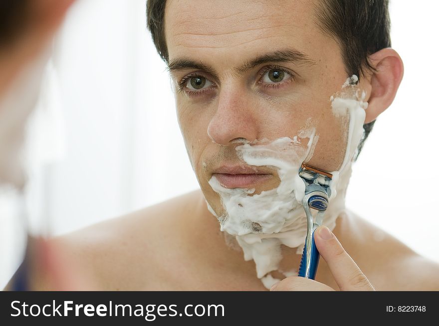 Young man shaving in the morning looking into mirror