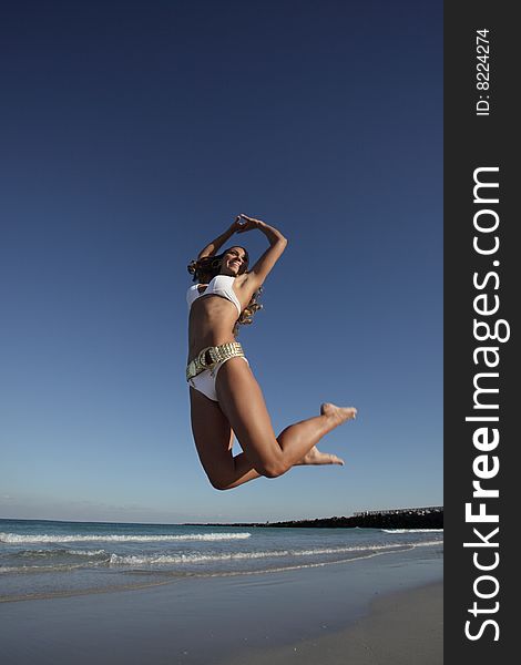 Young woman jumping on the beach on a deep blue sky. Young woman jumping on the beach on a deep blue sky