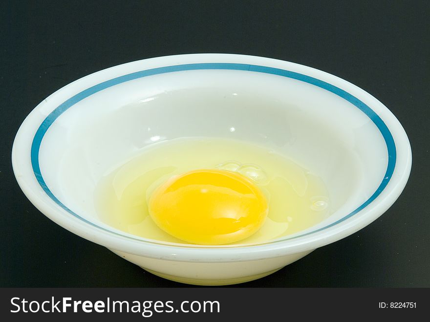 Broken egg in a small bowl on blackground.