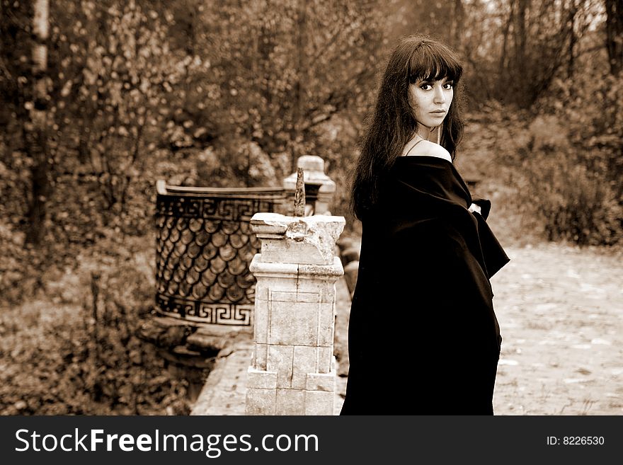 Girl in fall park in old bridge, sepia toned