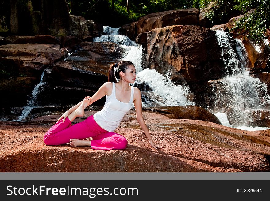 Outdoor young woman sitting by the waterfall doing yoga. Outdoor young woman sitting by the waterfall doing yoga