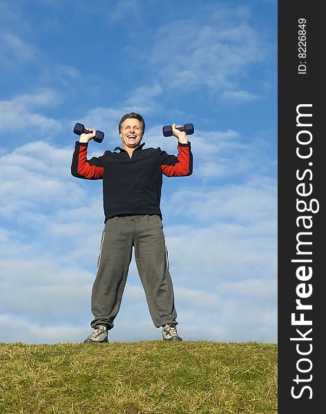 A handsome forties man is standing on the grass with and performing dumbell presses. A handsome forties man is standing on the grass with and performing dumbell presses