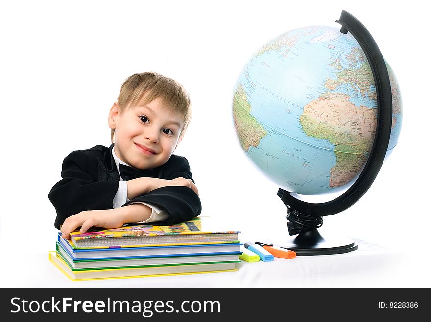 Happy little schoolboy sitting by the table with a globe and a lot of books. Happy little schoolboy sitting by the table with a globe and a lot of books