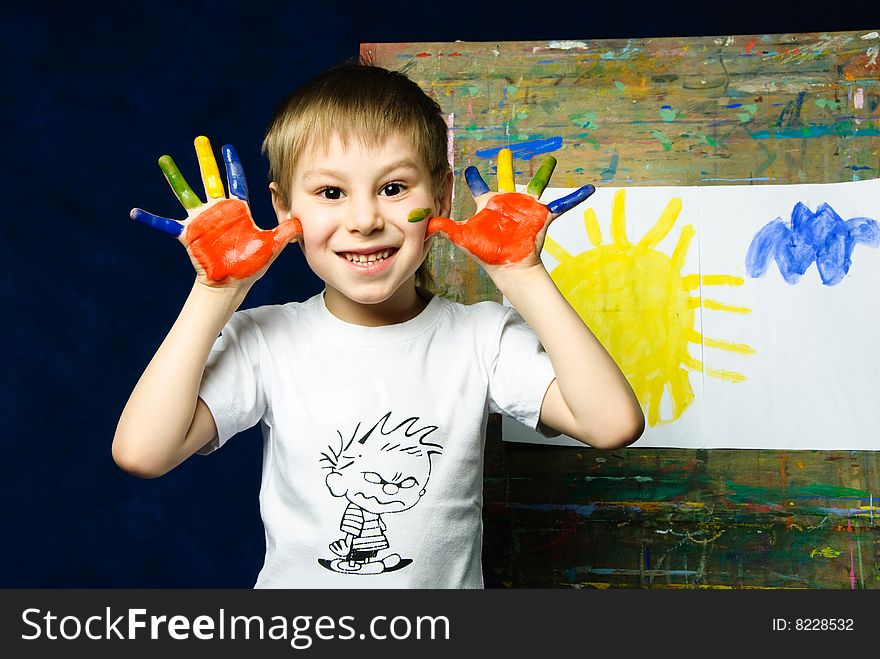 Cheerful little boy standing near the easel and showing his dirty fingers. Cheerful little boy standing near the easel and showing his dirty fingers