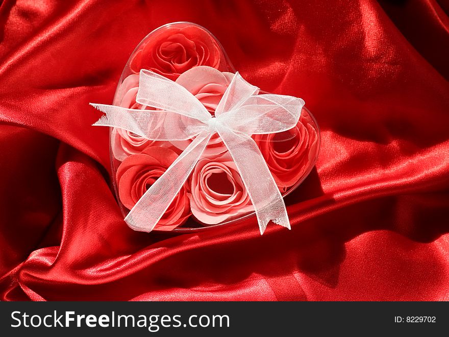 Roses in a box in shape of heart on bright red satin fabric. Roses in a box in shape of heart on bright red satin fabric