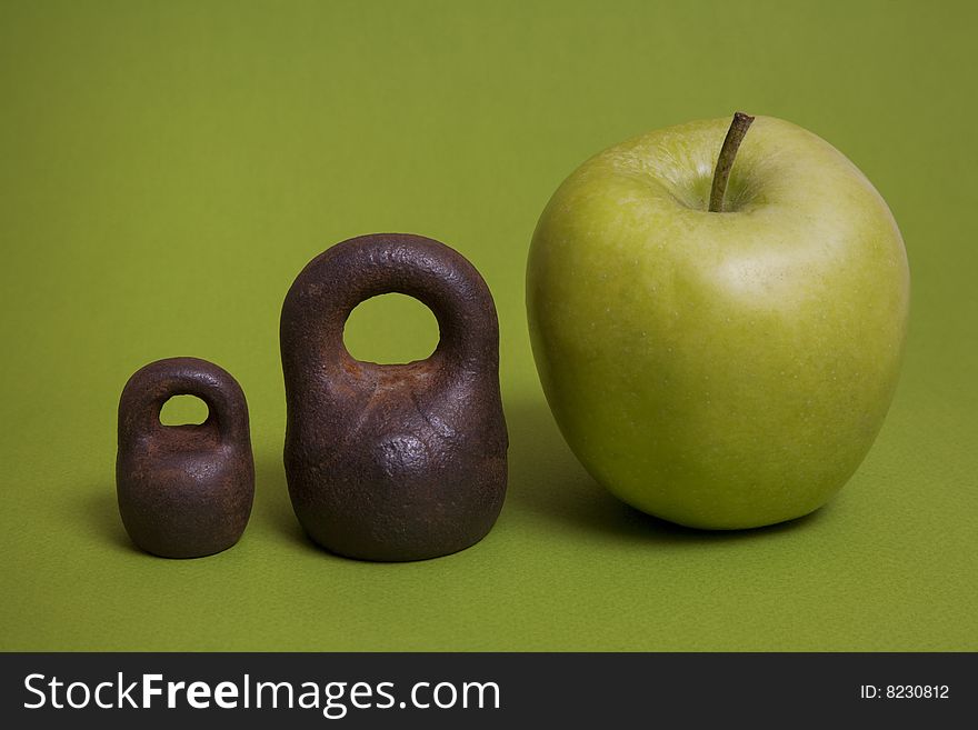 Two mini weights and one apple on a green background. Two mini weights and one apple on a green background