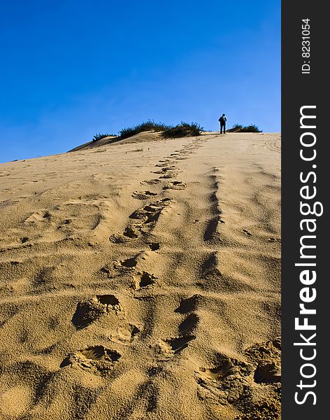 A man going up alone to the top of a sandy hill. A man going up alone to the top of a sandy hill.