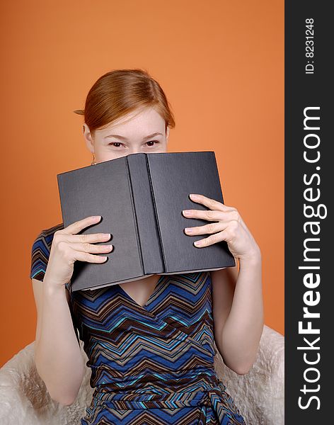 Young woman sits in an armchair and hides the face behind the book. Young woman sits in an armchair and hides the face behind the book